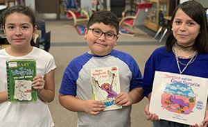 Three young students hold books out to the camera
